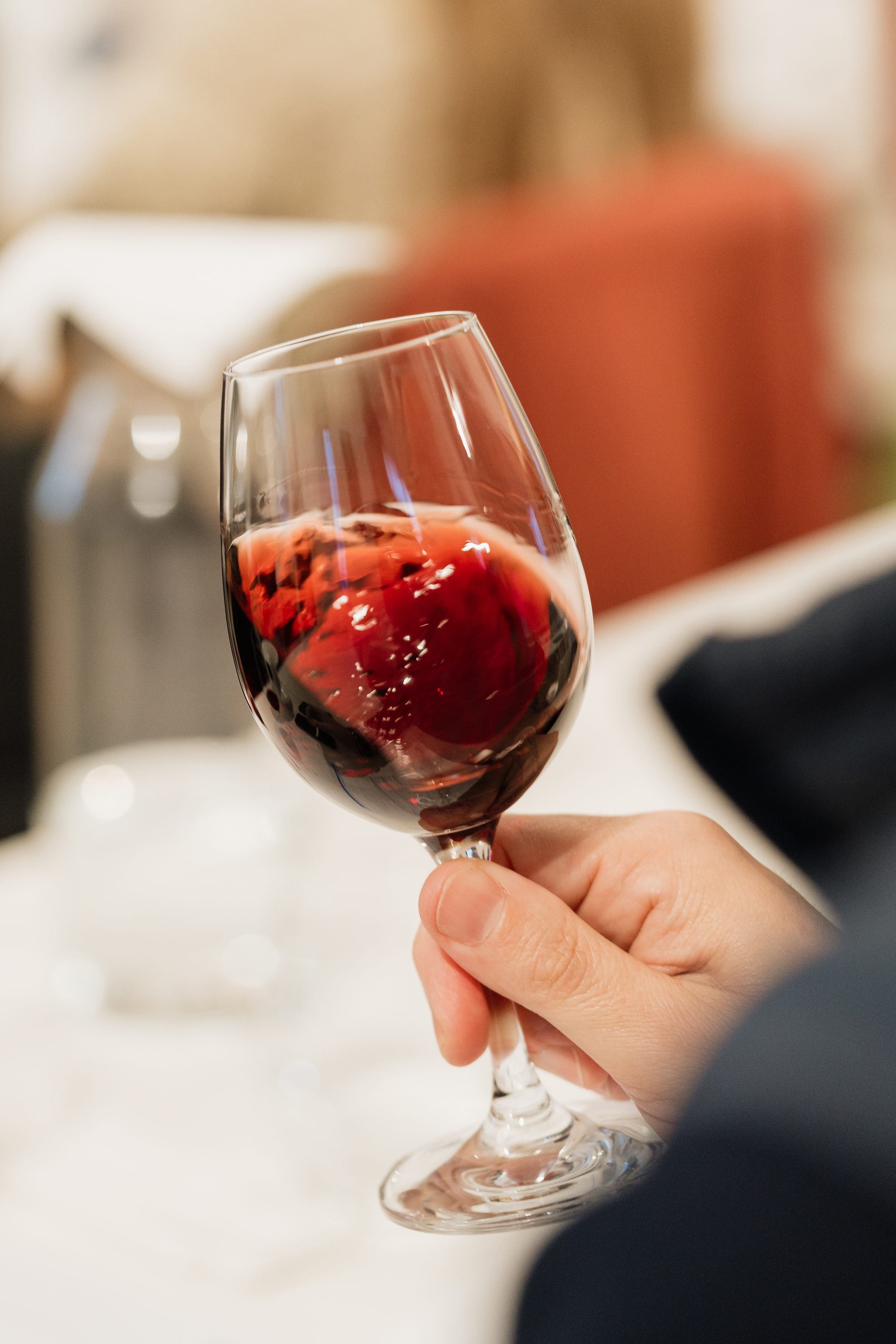 Uma mão segura um copo de vinho tinto, que está a ser agitado, num ambiente de degustação ou evento