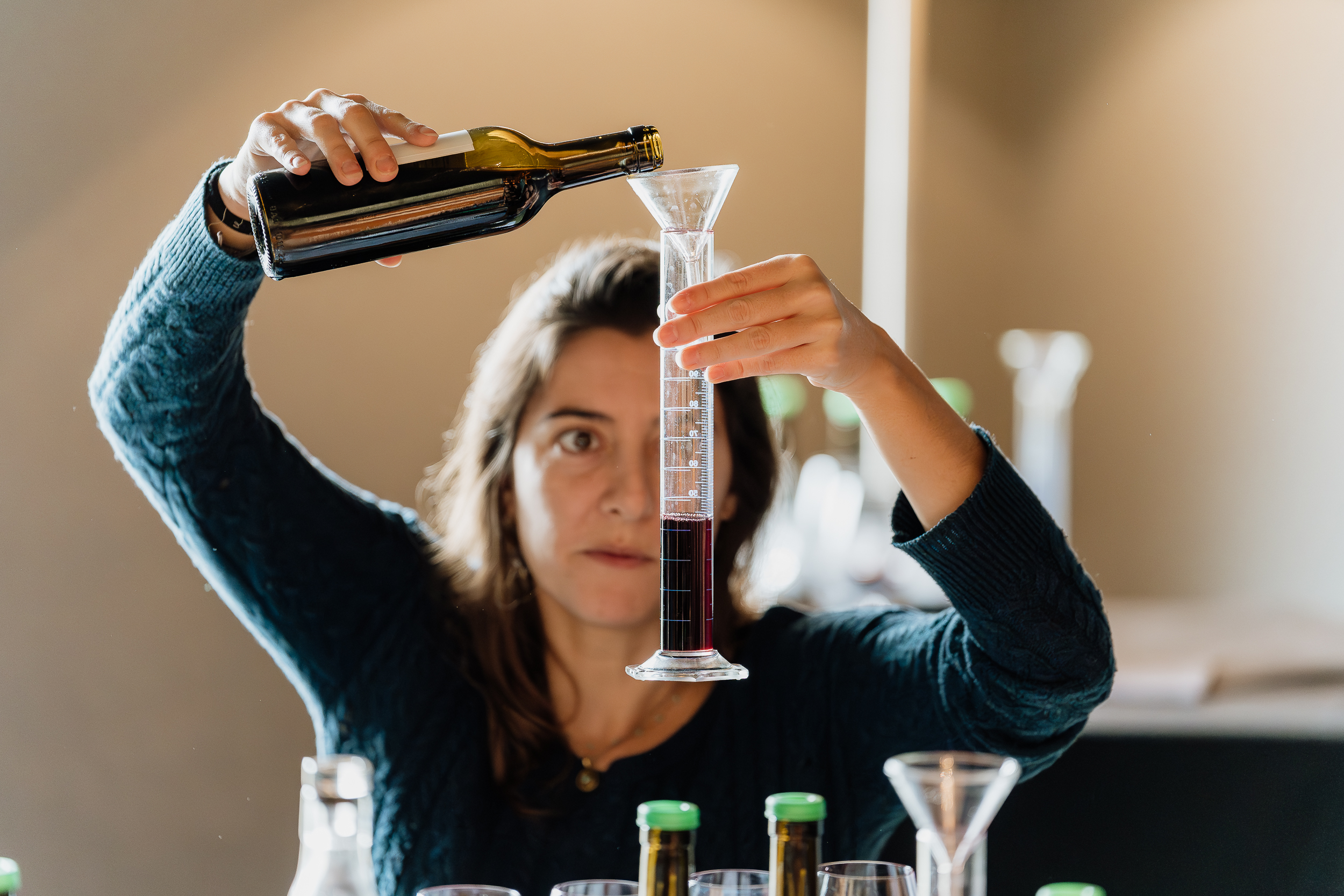 Uma mulher está a verter vinho de uma garrafa para uma proveta