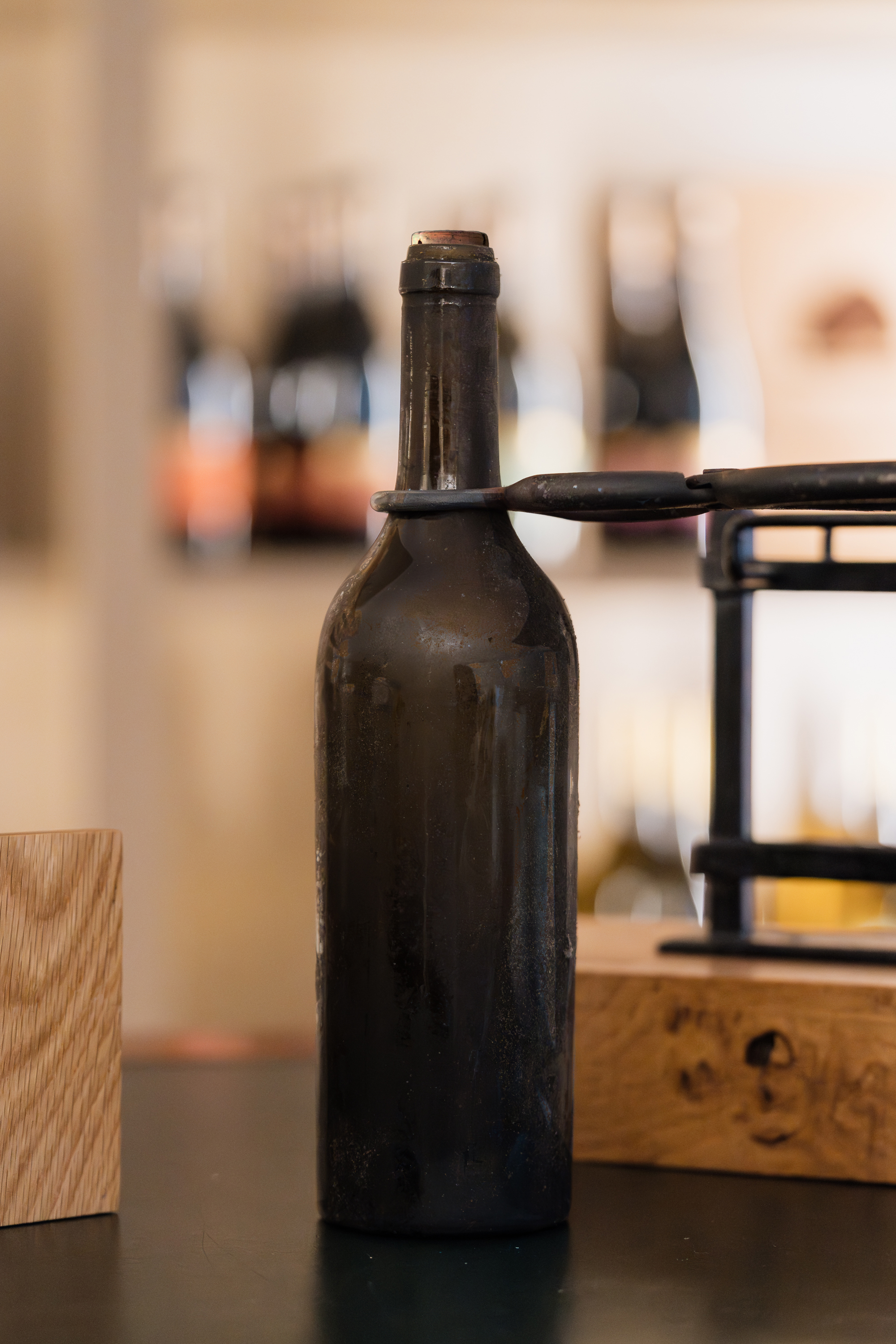 uma garrafa de vinho antiga e empoeirada sobre uma mesa, com garrafas desfocadas ao fundo