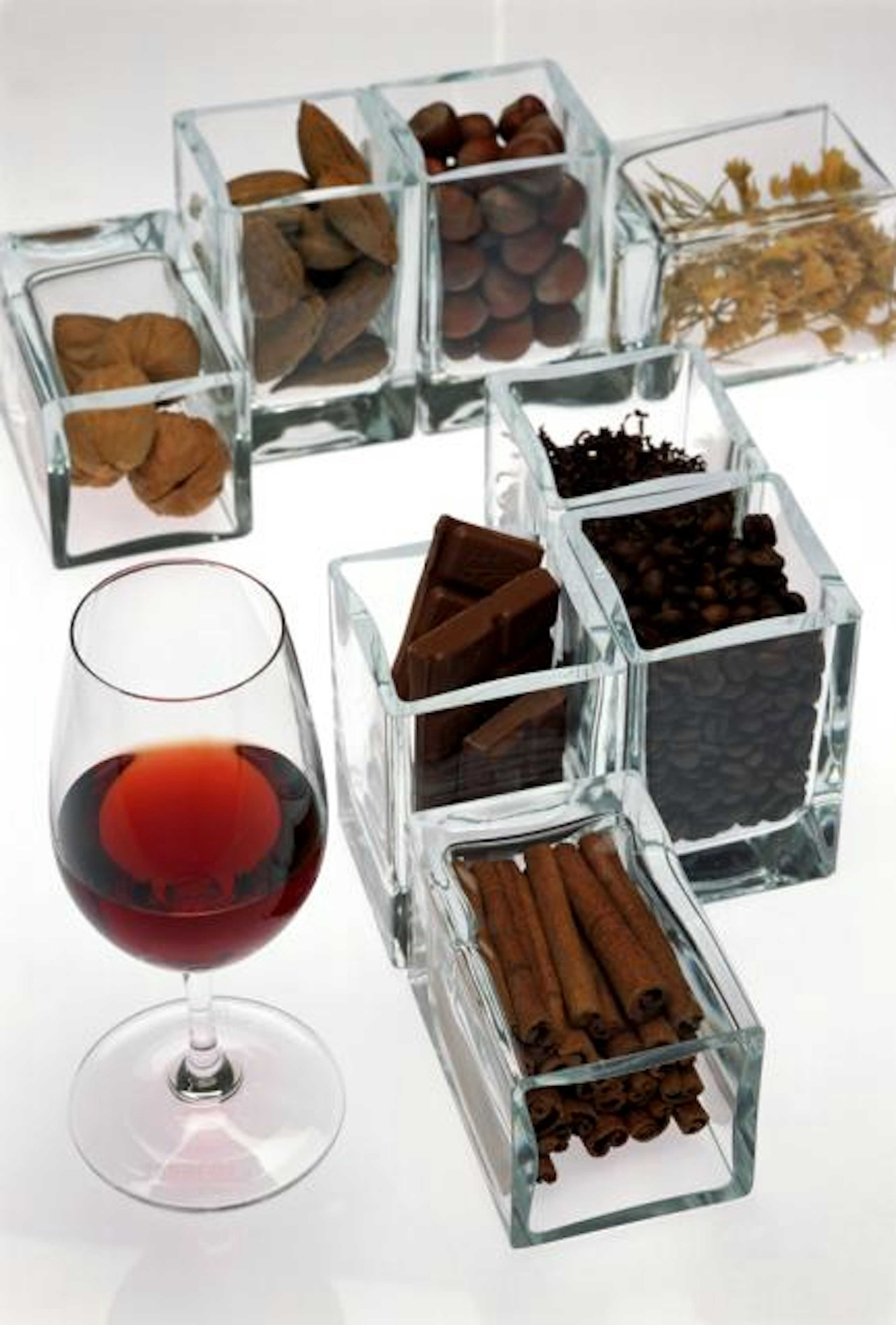 Um copo de vinho tinto está rodeado por vários ingredientes em recipientes de vidro, como nozes, amêndoas, avelãs, café, chocolate e canela