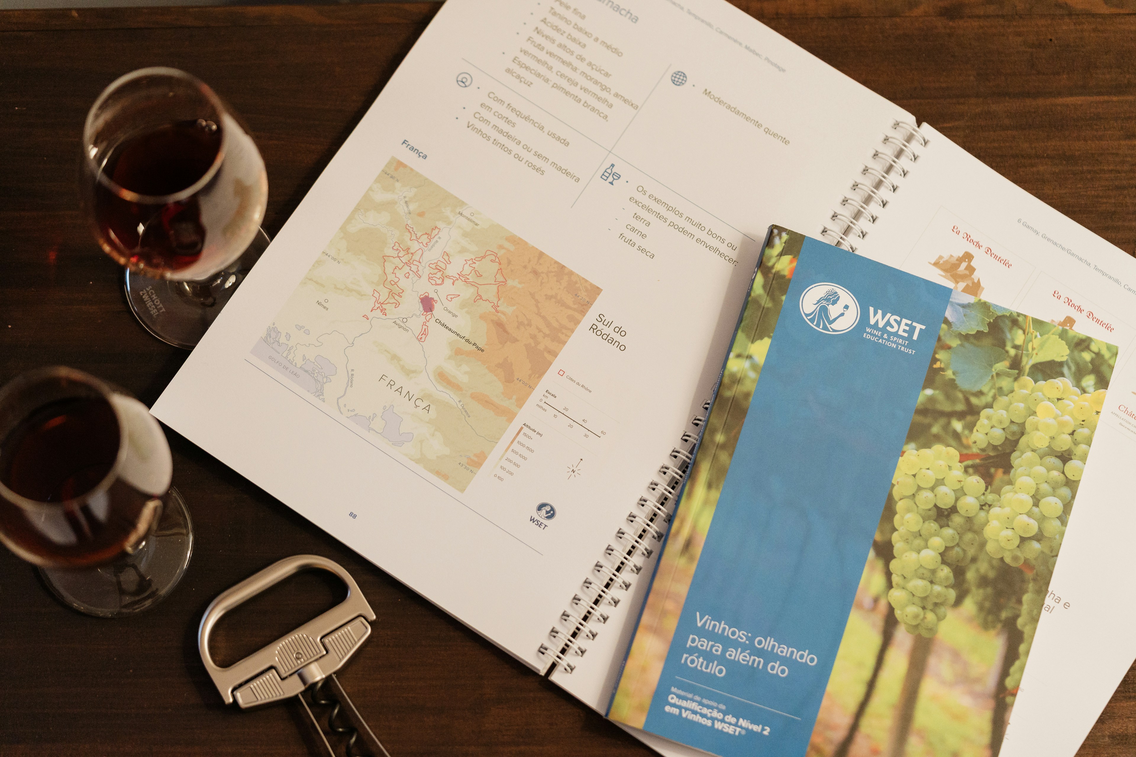 Two wine glasses, a corkscrew, and wine study materials on a table