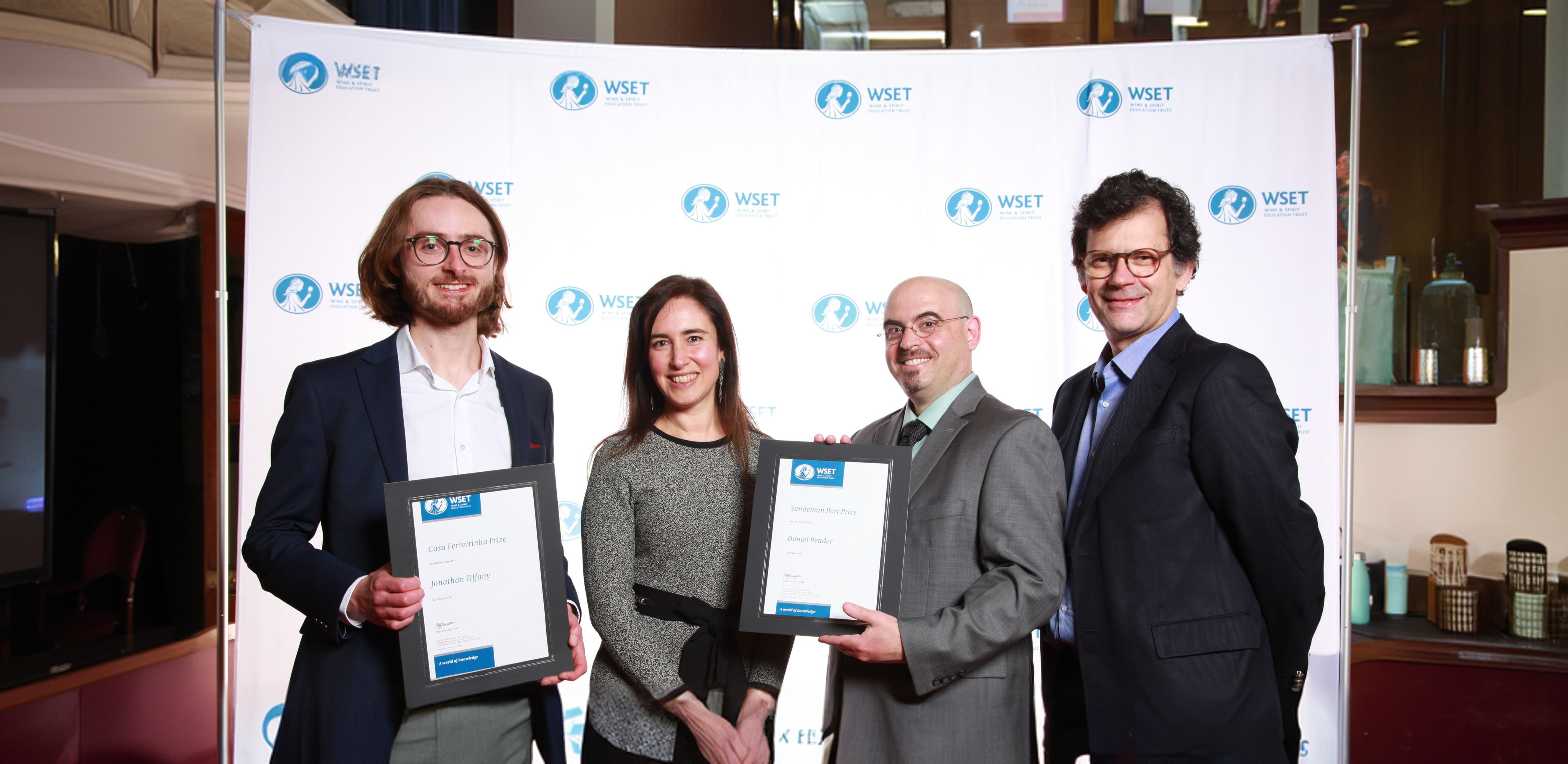 Quatro pessoas sorridentes posam para uma foto, com duas delas a segurar diplomas da WSET