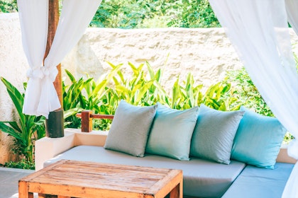 Patio with plants, white adobe wall and curtains, light blue couch, and coffee table