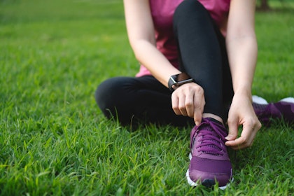 Woman sitting on lawn in workout clothes tying her sneaker