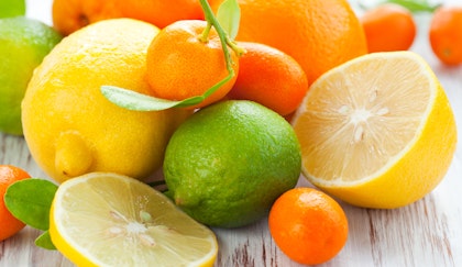 Assorted citrus fruits such as lemons, limes oranges, kumquats are shown whole, in halves and sliced, on a wooden table.