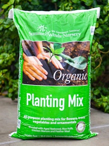 2 cu ft. bag of summerwinds nursery planting mix sitting on the sidewalk in front of green shrub