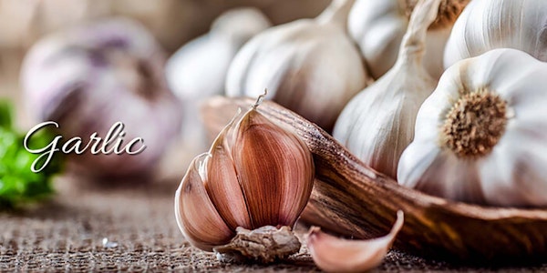 Whole garlic bulbs in a bowl to the right and some in the background with a half of one sitting out of the bowl in the front and a garlic bulb split off with the word "garlic" on the image