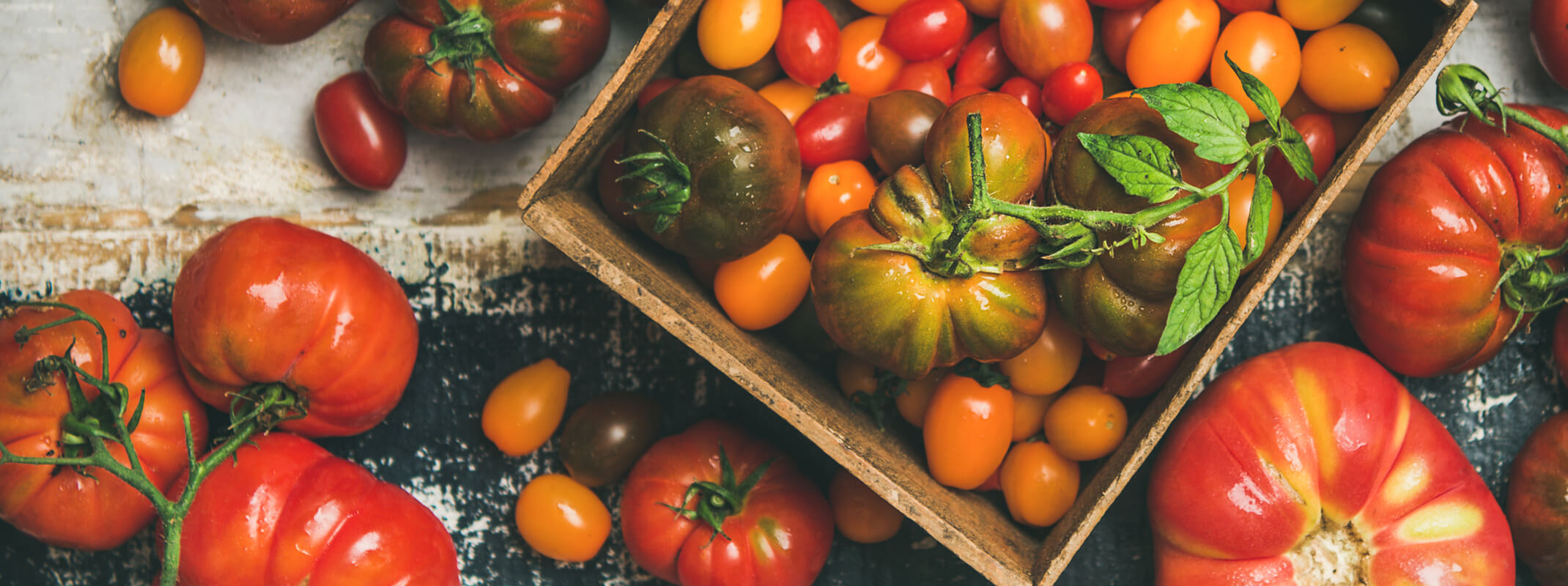 A variety of tomatoes, including heirlooms, on a wooden table and in a wooden box