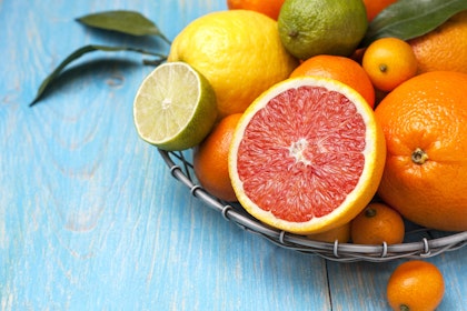 A variety of citrus fruits in a wire basket on a blue wooden table