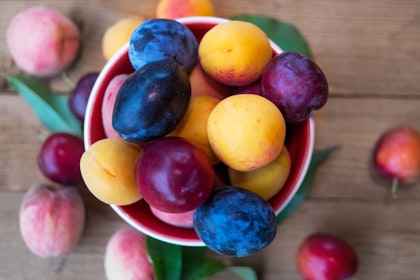 A variety of stone fruits in a bowl on a wooden table