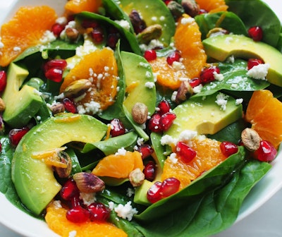 Sliced avocados in a mandarin salad with pomegranates, feta, seeds and spinach