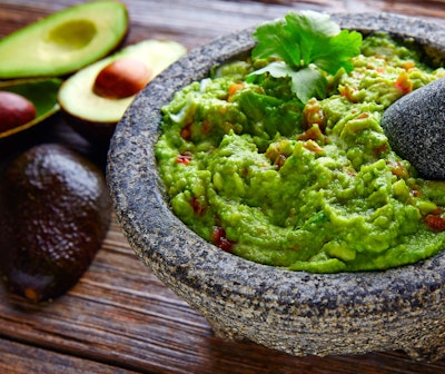 Guacamole in a guacamole molcajete with avocados cut in half and lying next to the bowl