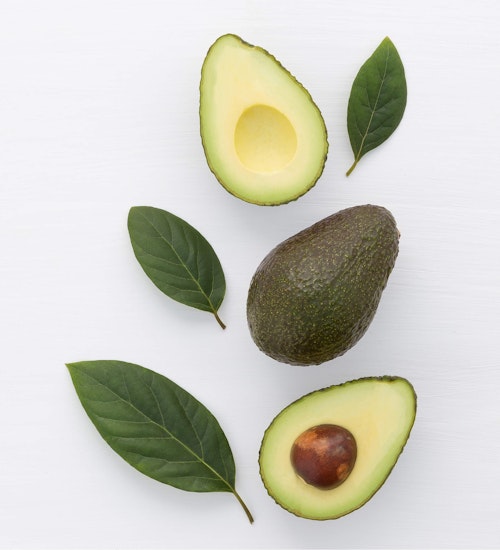 two half avocados, one whole and aocado leaves layed in the shape of a leaf