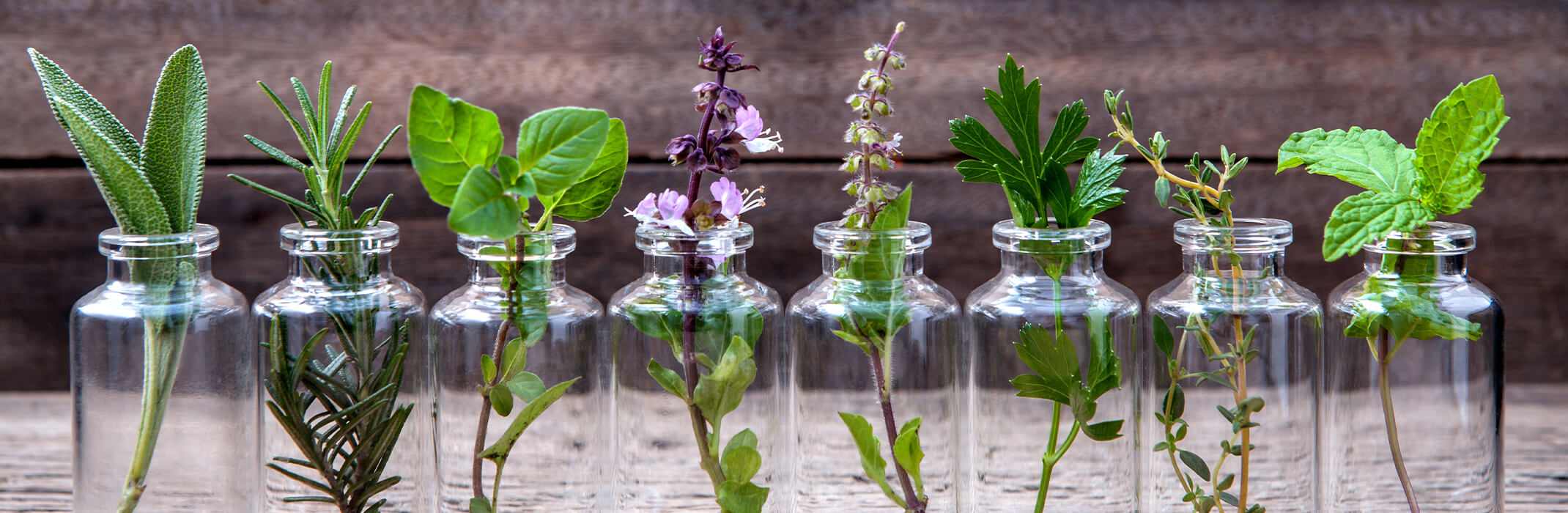 A variety of herbs - each in a clear glass bottle on a wooden table