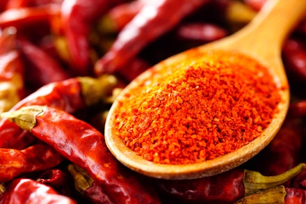 A wooden spoon of chili powder on top of dried whole chili peppers
