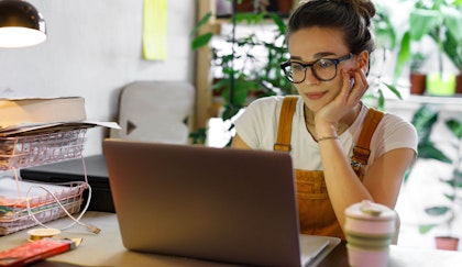 woman sitting at her computer and desk with houseplants blurred behind her