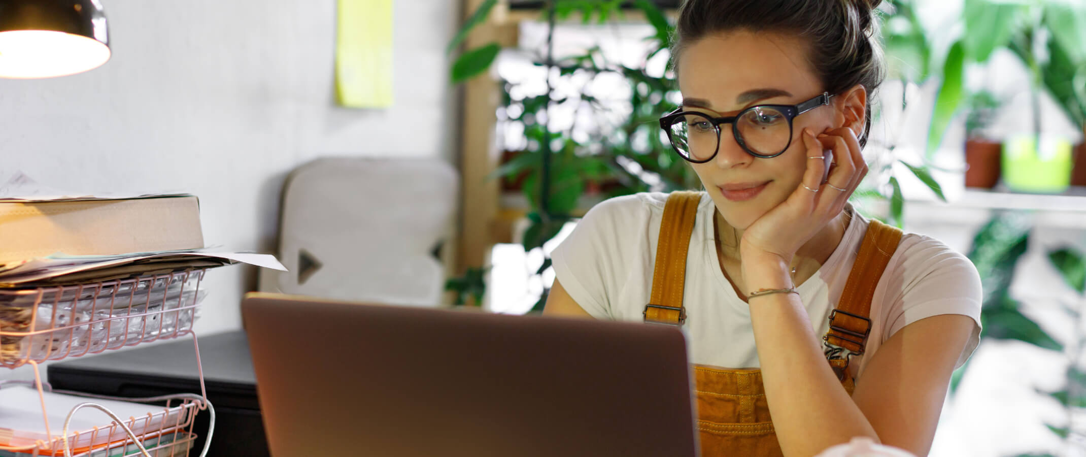 woman sitting at her computer and desk with houseplants blurred behind her