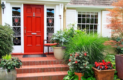 Front door of a home showing off beautiful landscape down brick steps with potted plants around