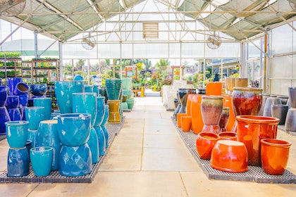 A variety of colorful outdoor ceramic pottery on display in a covered area at SummerWinds Nursery with plants in the background