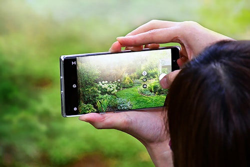 A person with dark hair taking a landscape photo on their cell phone of a beautiful landscape