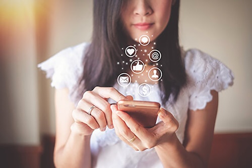social media on phone woman holding her cell phone scrolling through her social media with icons of social media popping up above the phone