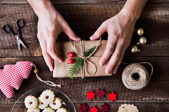 Creating a gift topper with an evergreen sprig, berries tied on with twine on a table with other decorative elements