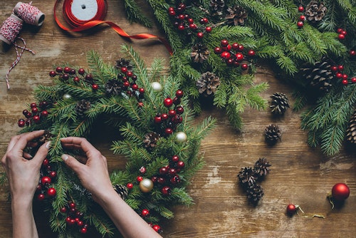 A woman  is putting together a holiday wreath with fresh greenery, berries and pinecones 