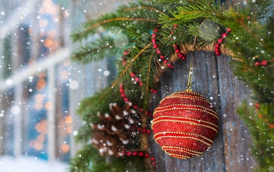 evergreen holiday wreath with red beads, pinecone, and a single ball ornament hanging on weathered shutter of window during a snowy day