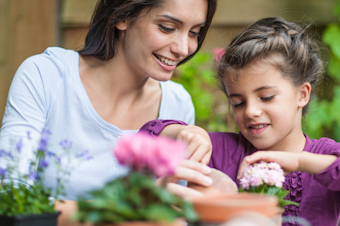 A woman and her daughter potting flowers at a table in the garden