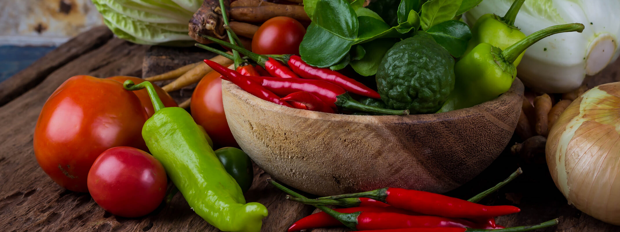 hot peppers tomatoes, onions and other veggies in and around wooden bowl