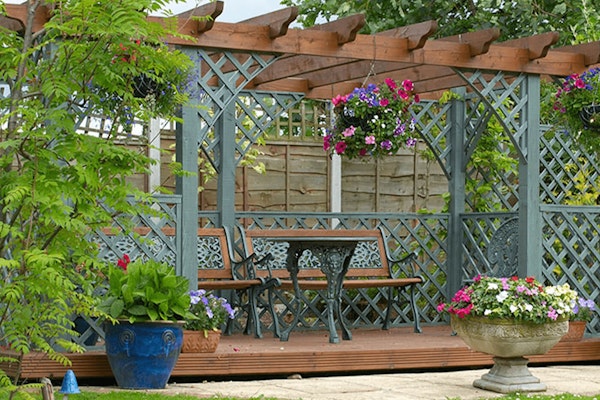 partial pergola with benches in garden surrounded by potted plants and trees