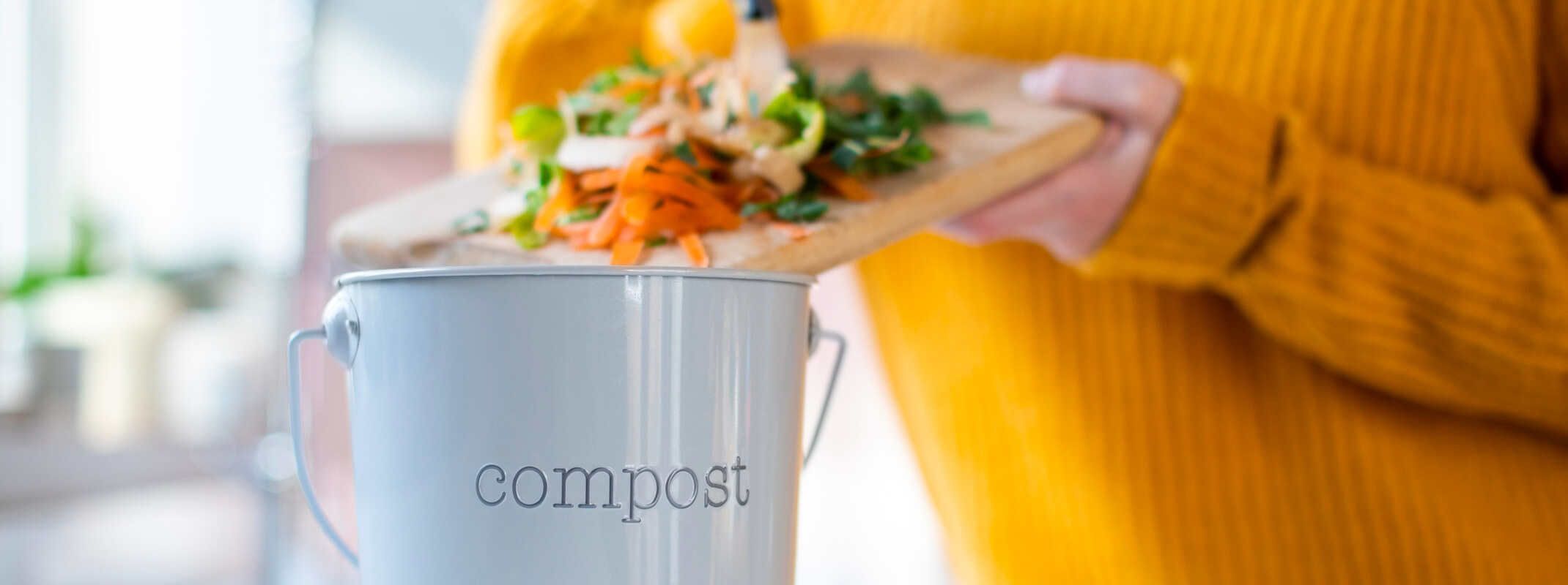 person scraping food scraps into a bucket that says compost