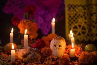 A Dia De Los Muertos (Day of the Dead) altar with flowers, food, candles, flags and a skull.