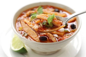 A bowl of tortilla soup with a lime on the side.