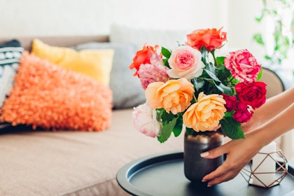 A bouquet of fresh cut roses on a black side table in a living room with colorful pillows.