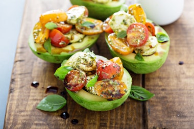 A wooden table with 4 caprese-stuffed avocado halves.