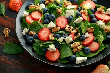 A salad made with strawberries, blueberries, feta cheese, spinach and walnuts.