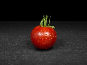 A single stupice tomato on a charcoal-colored table.