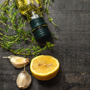 Lemon, garlic, oregano and a bottle of oil on a dark wood table.