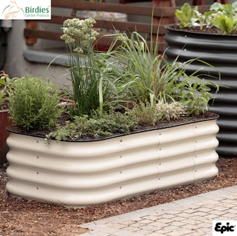 A light sand color Birdie metal raised garden bed in the garden.