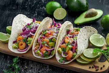 3 Cilantro Lime Shrimp Tacos on a cutting board surrounded by its ingredients.