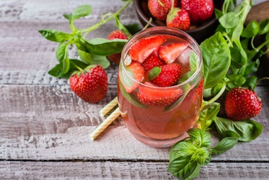 Basil Strawberry Iced Tea on a wooden table with fresh basil and strawberries.