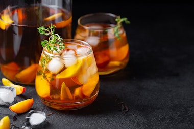 Peach Thyme Iced Tea on a stone table with ice cubes and sliced peaches.
