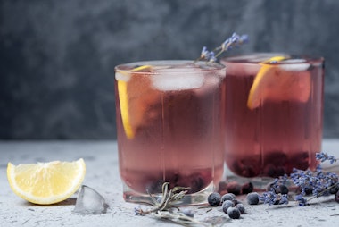Lavender Blueberry Spritzer on a table with fresh lemon, lavender and an ice cube.