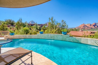Luxury pool overlooking desert mountains with potted plants, seating and an umbrella.