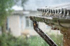 rain pouring on metal roof of home and spilling over into gutter