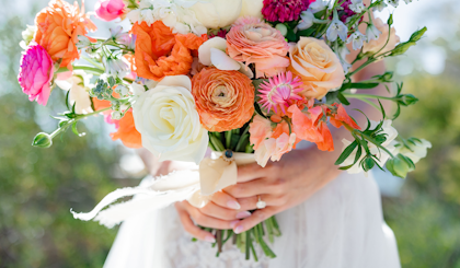 A bride holding a beautiful bouquet of white, orange and pink roses and other flowers.