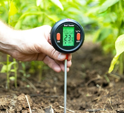 a man holding a soil tester stuck in the dirt