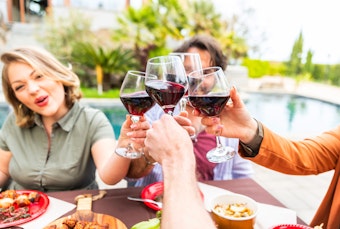 People toasting and enjoying wine, dining outside near a pool.