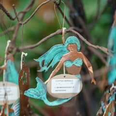 Dos Damas Mermaid Ornament hanging on some branches.